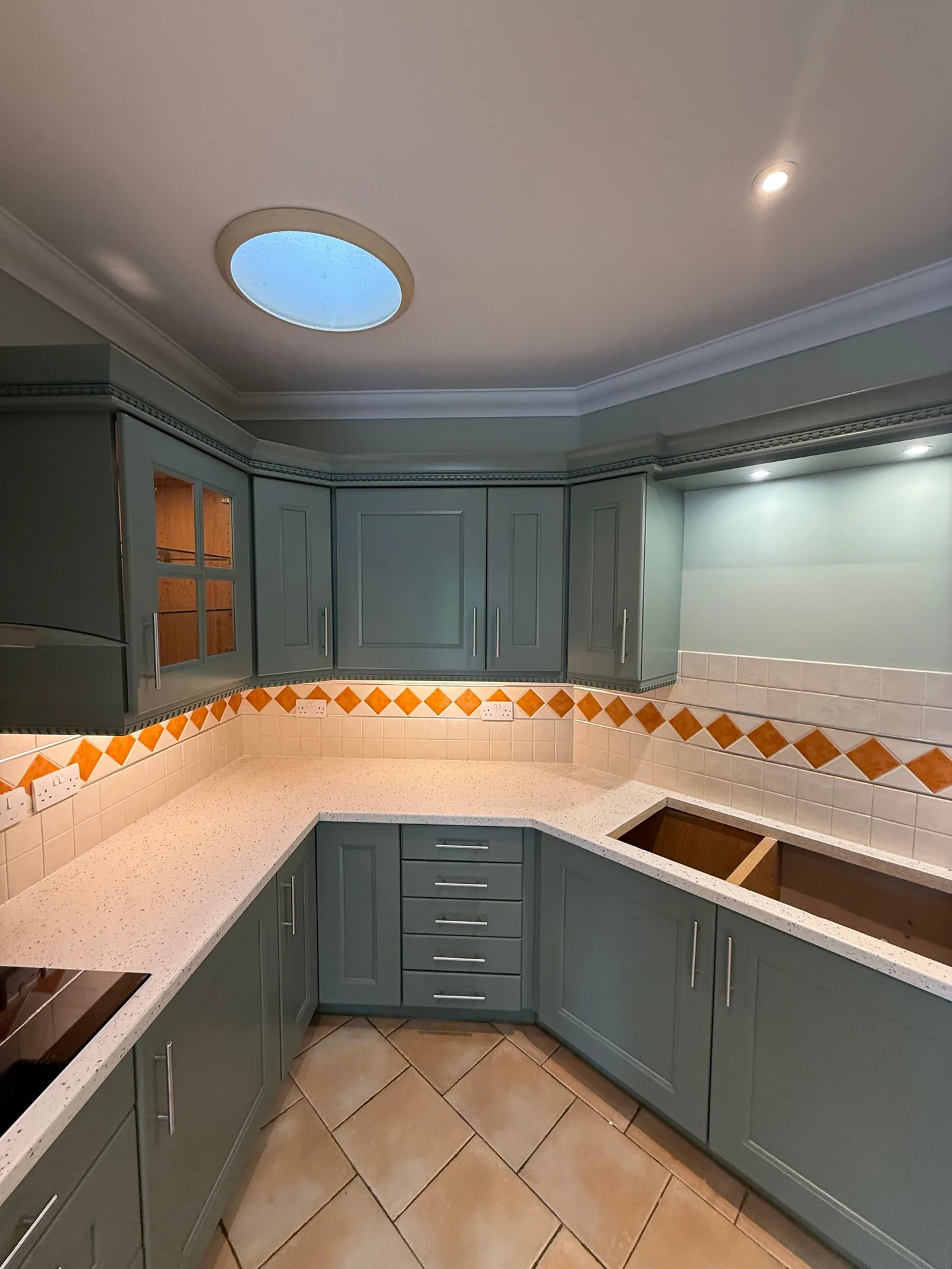 Sage green kitchen with a cream worktop and terracotta floor